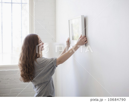 Young woman hanging picture on freshly painted wall 10684790