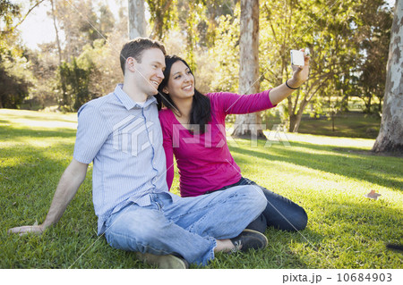 Couple sitting on grass in park photographing themselves Couple sitting on grass in park photographing themselves 10684903