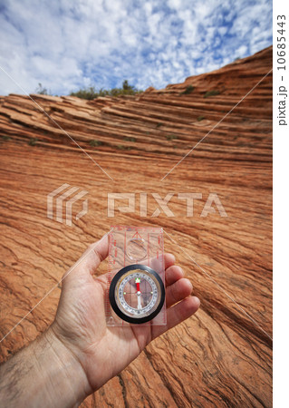 Human hand holding compass against eroded sandstone 10685443