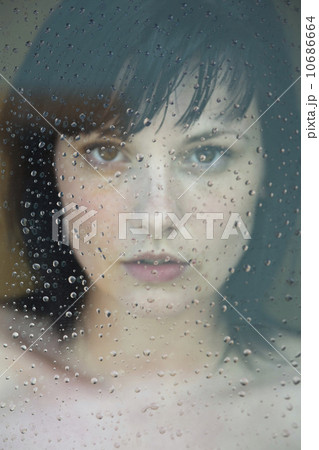 Naked young woman standing behind glass covered in raindrops Naked young woman standing behind glass covered in raindrops 10686664