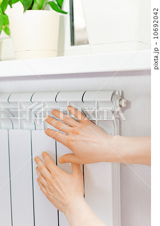 Arm put on  heating white radiator.Windowsill with flowers. 10692042