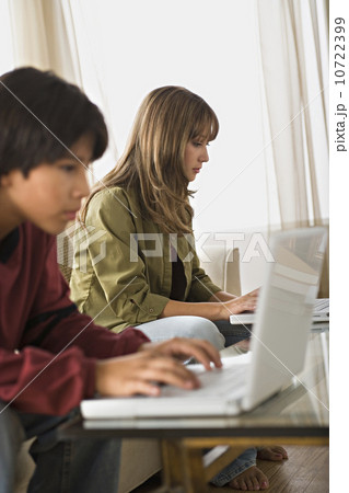 Brother and sister using laptops in living room 10722399