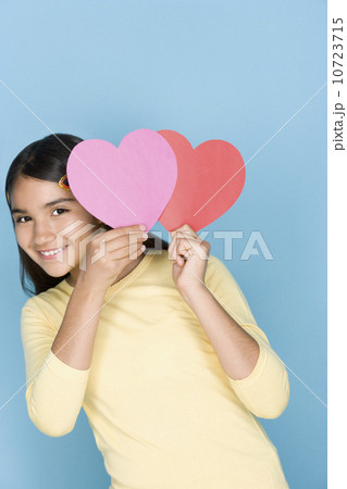 Studio shot portrait of teenage girl holding harts, waist up 10723715