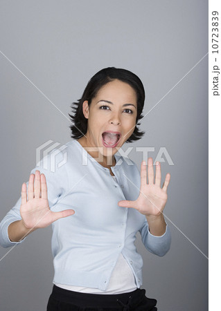 Studio shot portrait of mid adult woman with arms raised and open mouth, waist up 10723839
