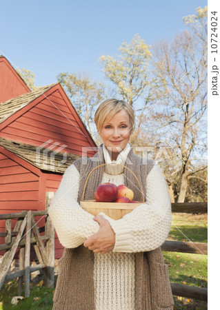 USA, New Jersey, Portrait of smiling woman holding basket with apples in front of cottage house in Autumn USA, New Jersey, Portrait of smiling woman holding basket with apples in front of cottage house in Autumn 10724024