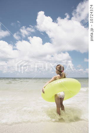 Girl carrying inflatable ring into ocean 10724374