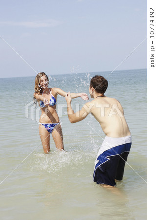 Teenage couple splashing each other in ocean 10724392