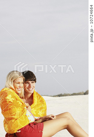 Young couple cuddling under towel on beach 10724664