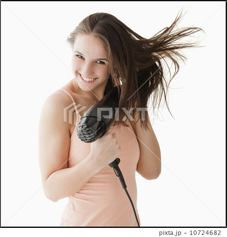 Studio portrait of young woman blow drying hair Studio portrait of young woman blow drying hair 10724682