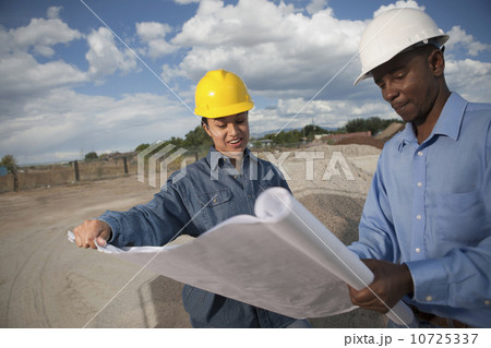 Two construction workers discussing blueprints on building site 10725337
