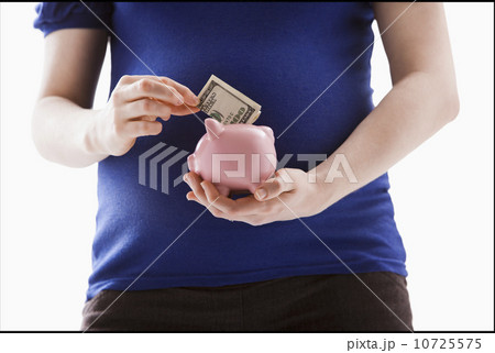 Studio Shot of mid section of pregnant woman putting money into Piggy Bank 10725575