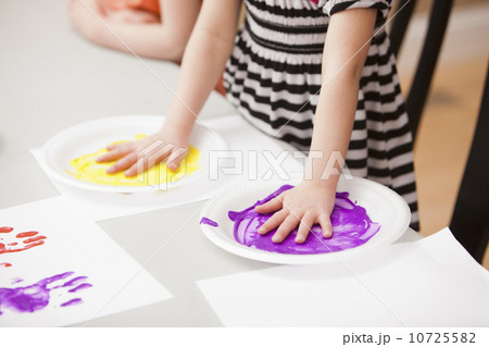 Girl (4-5) holding her hands on plates with paint 10725582