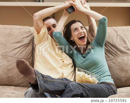 Front view of mid adult couple sitting on couch and fighting for remote control 10725591