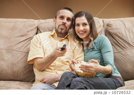 Front view of mid adult couple sitting on couch with remote control and popcorn 10726532
