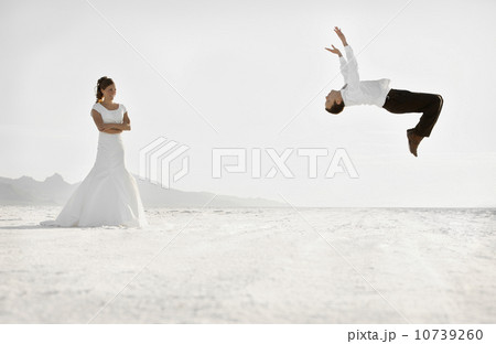 Bride watching groom performing backflip in desert Bride watching groom performing backflip in desert 10739260