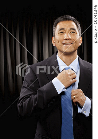 USA, Utah, Provo, Portrait of businessman standing in front of black curtain and adjusting tie 10741346