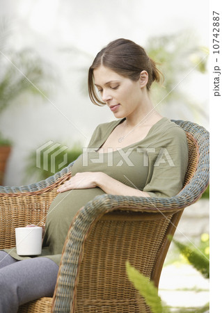 Pregnant woman sitting in wicker chair, touching belly Pregnant woman sitting in wicker chair, touching belly 10742887