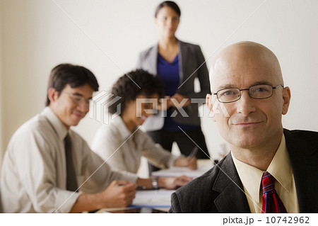 Mature businessman looking at camera, business team in background 10742962