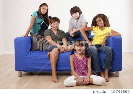 Group of children (10-11, 12-13) sitting on sofa, studio shot 10743860