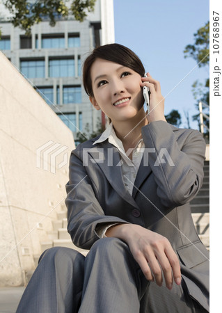 Smiling Asian business woman using cellphone and sit on stairs a 10768967