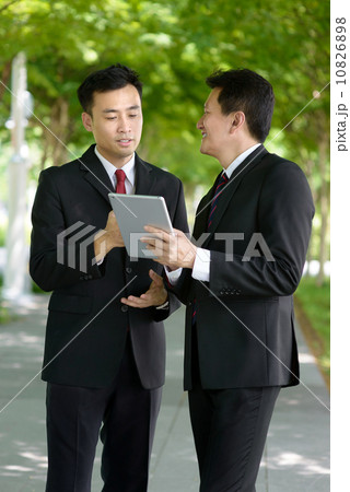 Two successful entrepreneur business men standing along promenade using mobile device tablet iPad  10826898