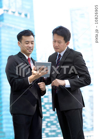 Two successful business men standing in front of glass building using mobile device tablet iPad  10826905