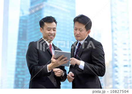 Two successful business men standing in front of glass building using mobile device tablet iPad Two successful business men standing in front of glass building using mobile device tablet iPad 10827504