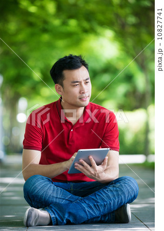 Young man in causal having an idea using iPad mobile device tablet seating along promenade Young man in causal having an idea using iPad mobile device tablet seating along promenade 10827741