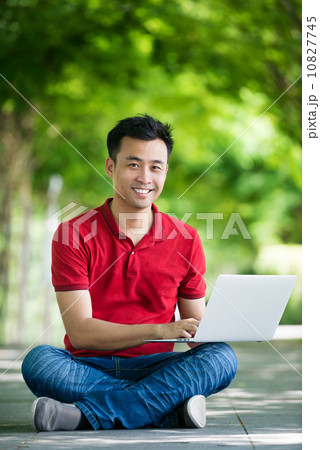 Young man in causal using mobile device laptop seating along promenade Young man in causal using mobile device laptop seating along promenade 10827745