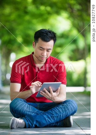Young man in causal having an idea using iPad mobile device tablet seating along promenade Young man in causal having an idea using iPad mobile device tablet seating along promenade 10827749