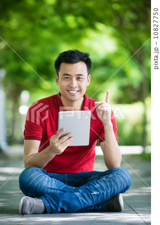 Young man in causal having an idea using iPad mobile device tablet seating along promenade Young man in causal having an idea using iPad mobile device tablet seating along promenade 10827750
