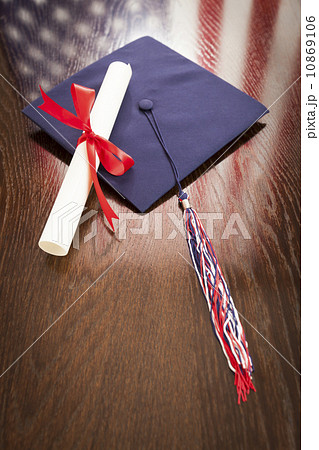 Graduation Cap and Diploma on Table with American Flag Reflectio 10869106