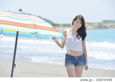 ビーチパラソルのわきに佇む若い女性 10870589