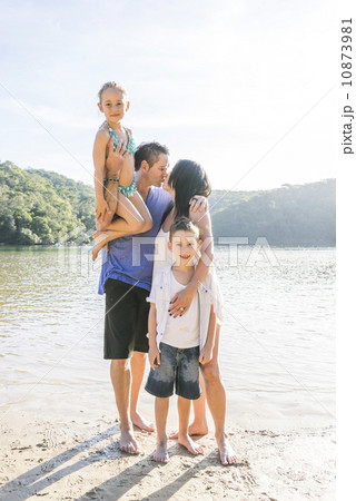 A Caucasian family standing together posing for a photo by the beach in the sun. A Caucasian family standing together posing for a photo by the beach in the sun. 10873981