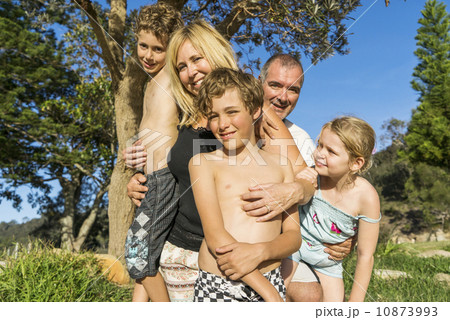 A Caucasian family standing together posing for a photo by the beach in the sun.  10873993