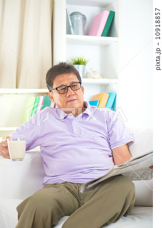 senior asian chinese  reading newspaper on a sofa in home 10918857