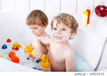 Two little twins boys having fun with water by taking bath in ba Two little twins boys having fun with water by taking bath in ba 10923542