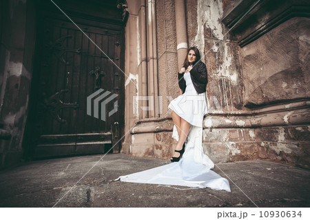 Woman in long white dress leaning against ancient wall of abbey 10930634