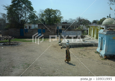 女性が水を入れた壺を頭に乗せて運んでいるカジュラーホーの農家 10931995