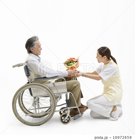 車椅子に乗る患者に花束を渡す看護士 10972659
