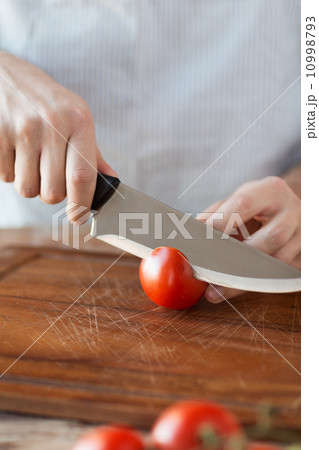 male hand cutting tomato on board with knife 10998793