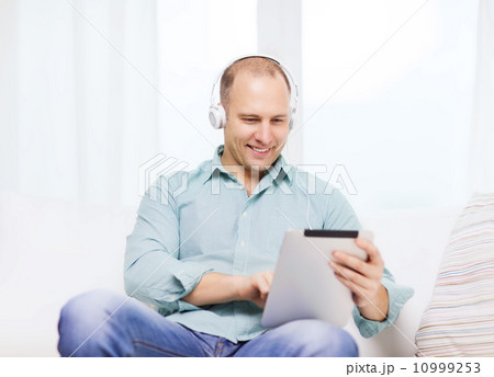 smiling man with tablet pc and headphones at home smiling man with tablet pc and headphones at home 10999253