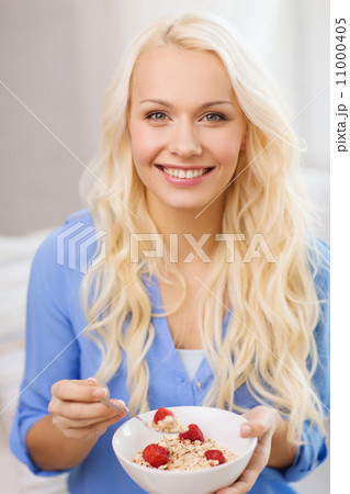 smiling woman with bowl of muesli having breakfast 11000405
