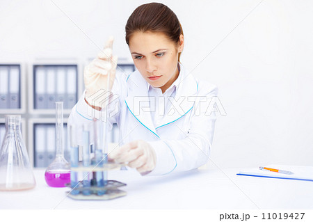 Young chemical female researcher with vials and flasks makes som Young chemical female researcher with vials and flasks makes som 11019427