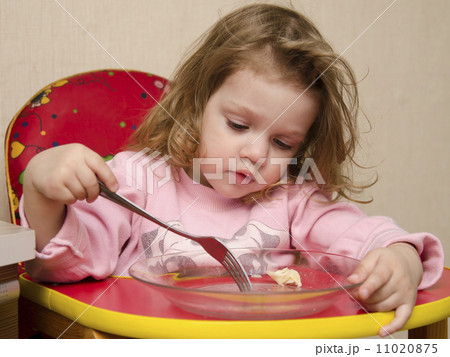 Two-year-old girl eats with a fork at table in kitchen Two-year-old girl eats with a fork at table in kitchen 11020875