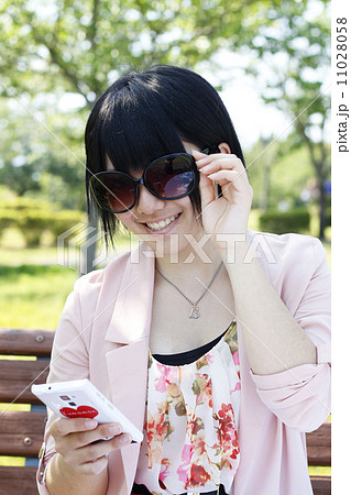 サングラスをかけスマホを見る女子高生の写真素材