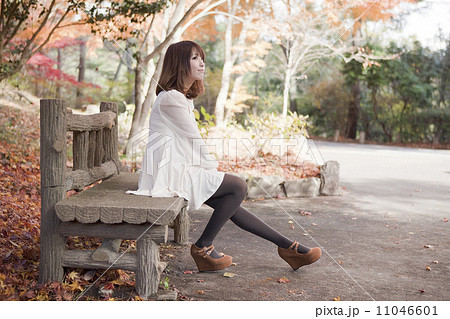 秋の紅葉した公園のベンチで座っている女性の写真素材