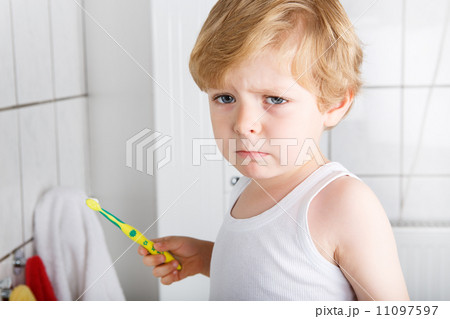 Lovely toddler with blue eyes and blond hair brushing his teeth 11097597