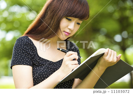 Beautiful young teenage female student reading and writing in park 11103072
