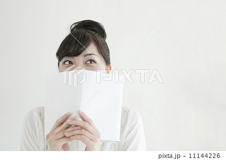 本で顔を隠す若い女性の写真素材